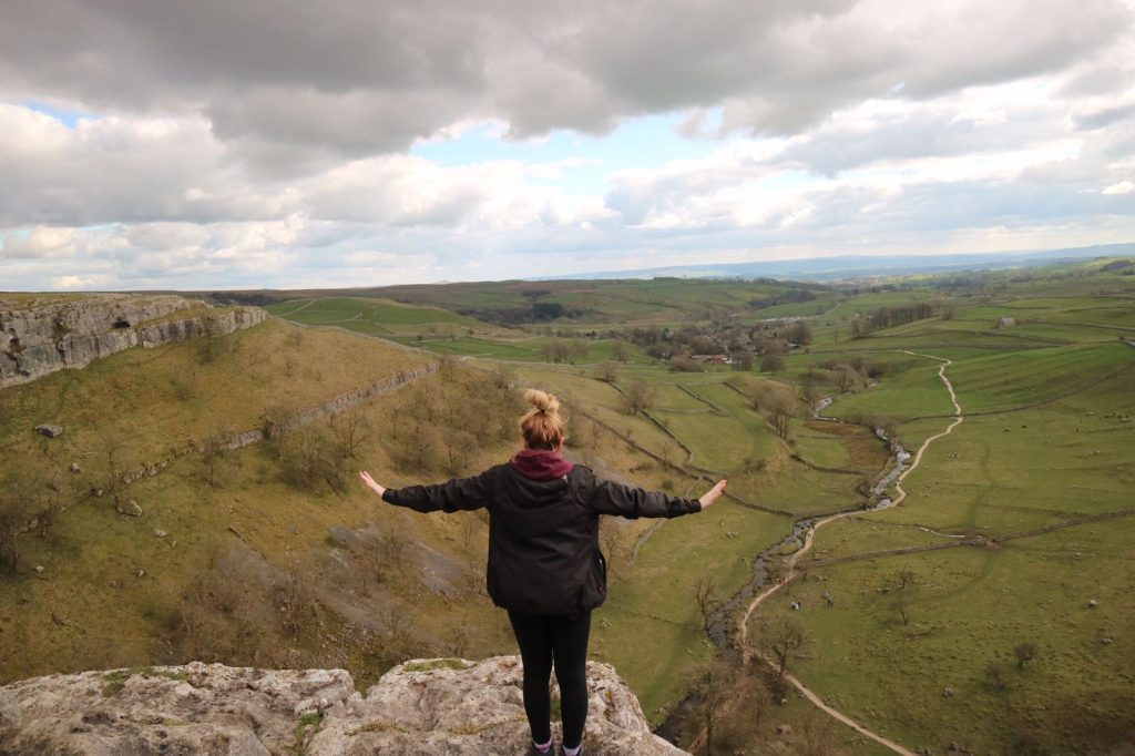 Woman with open arms on the edge of Malham Cove, looking over the valley