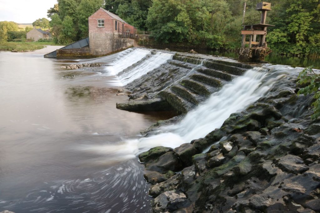 Small waterfalls next to red brick hydroelectric plant building