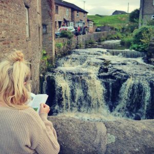 Woman looking at walking guide in front of Hawes waterfall