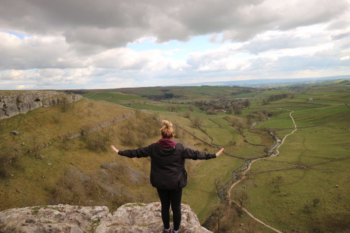 Woman on edge of Malham Cove, looking over valley