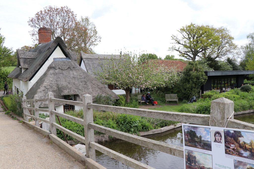 Thatched roof cottage next to a wooden bridge and river