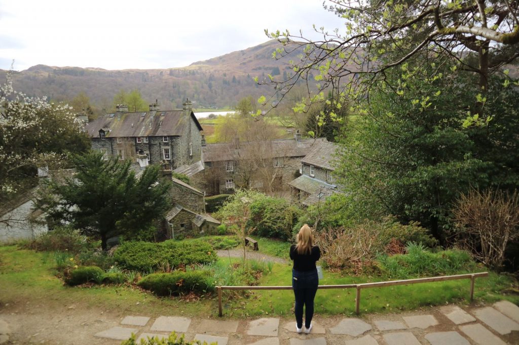 Woman looking at grey stone buildings and Grasmere in the distance